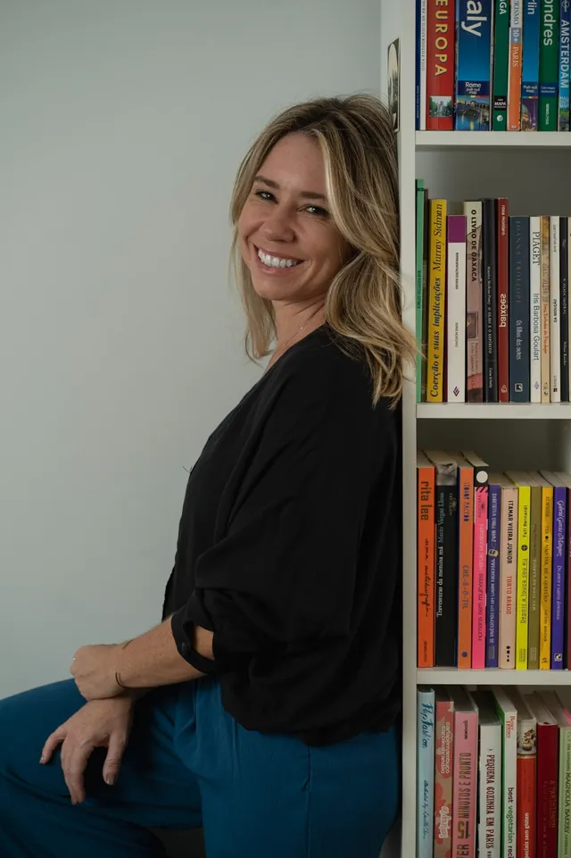 Milena Alves de Carvalho, psicóloga, sorrindo encostada numa estante de livros